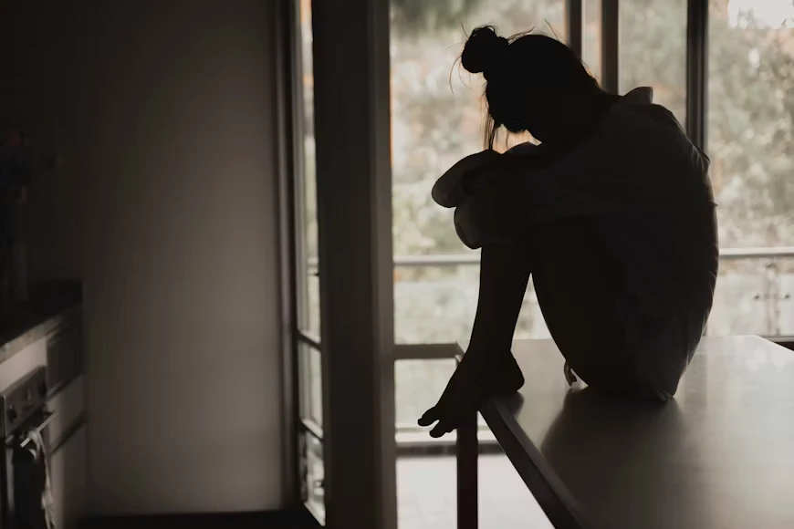 Woman sitting alone by a window, showing how trauma can lead to withdrawal